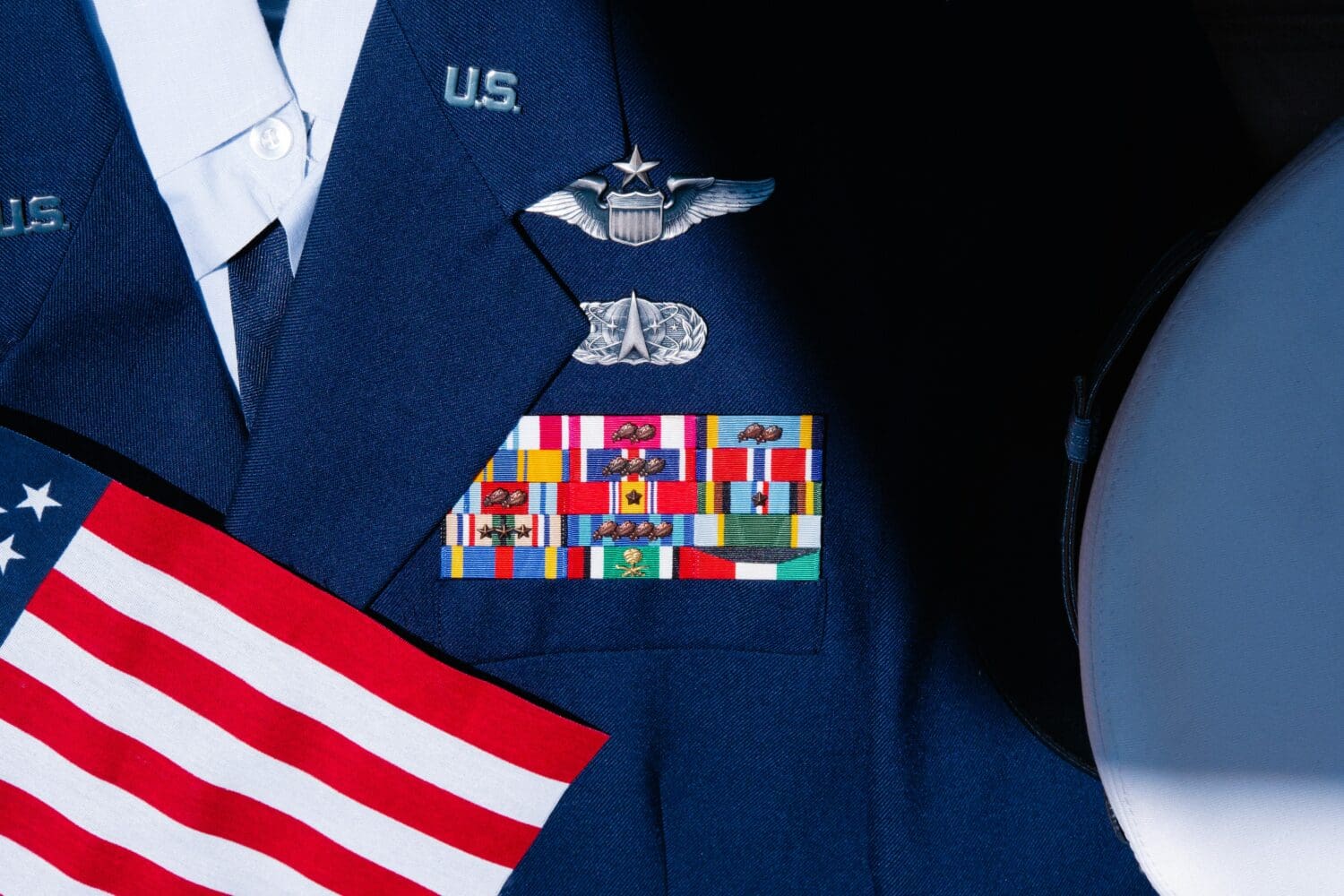 A decorated U.S. Air Force service dress uniform displayed with command pilot wings, a full ribbon rack, a service cap, and an American flag.