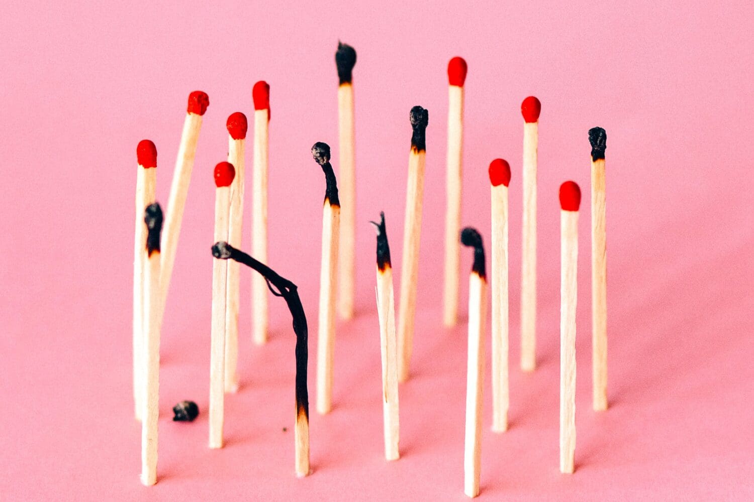Row of burned and unburned matches against a pink background, symbolizing MBA application burnout and the need to manage stress before it spreads.