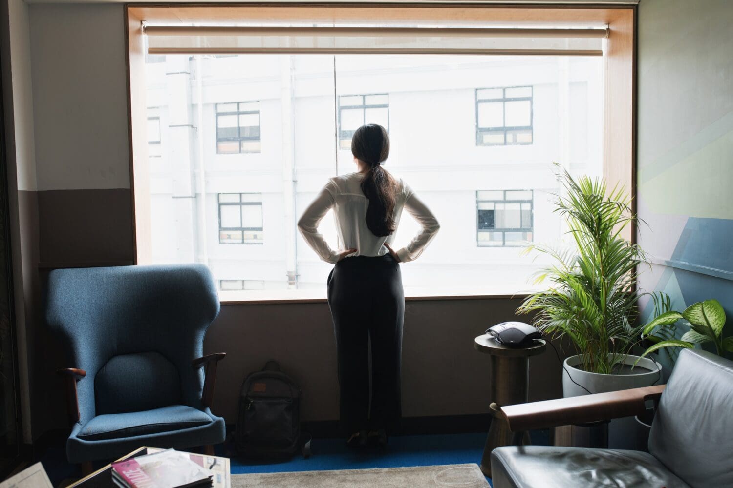Older MBA applicant standing in a modern office, looking out the window while considering her next career step.