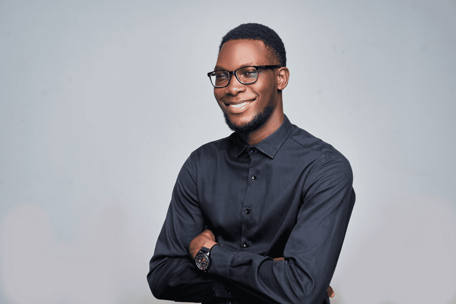 Smiling professional with arms crossed, wearing glasses and a dark shirt.