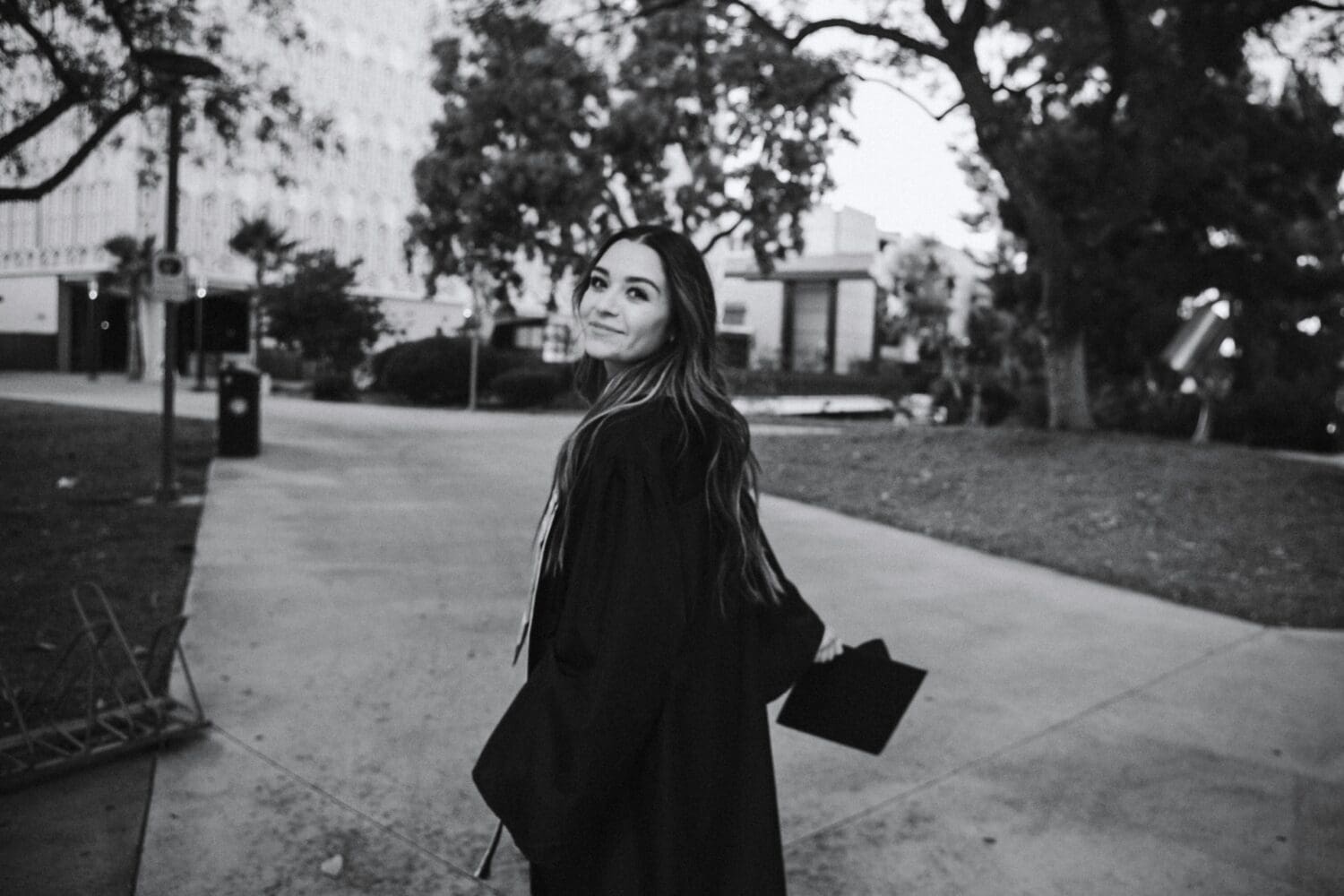 College senior in graduation gown considering next steps, including deferred MBA programs.