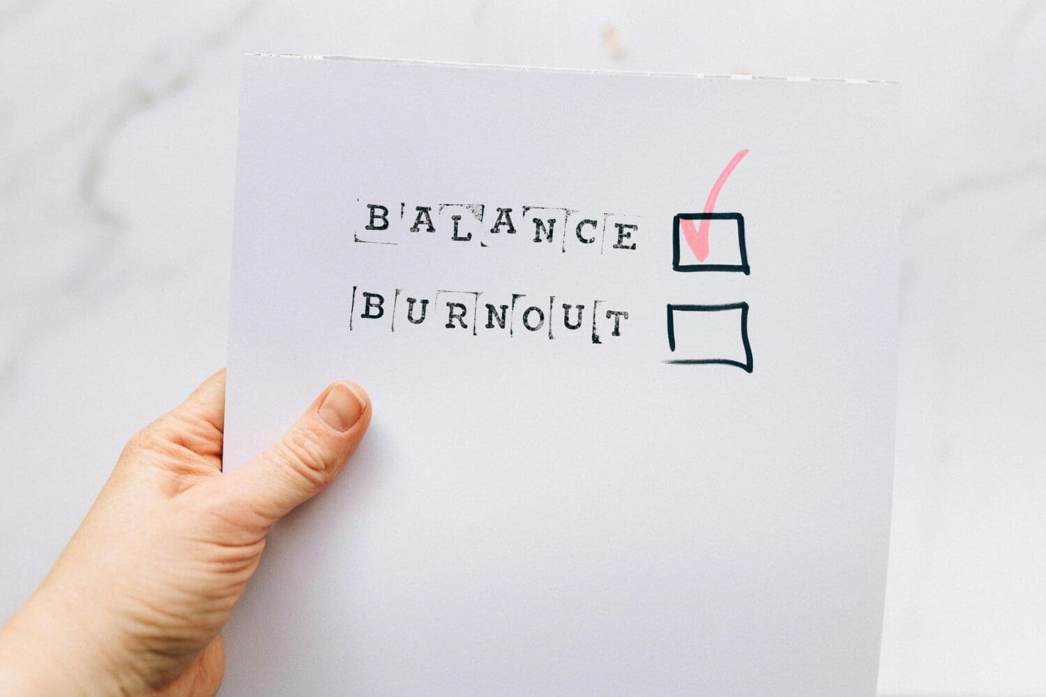 Hand holding paper with checkboxes labeled balance and burnout, with balance checked, symbolizing managing MBA application stress and avoiding burnout.