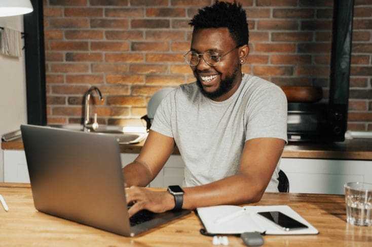 Smiling man working on laptop to create an MBA preparation timeline.