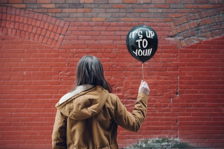 Person holding a balloon reading ‘It’s up to you,’ symbolizing the decision between taking the GMAT or GRE for MBA admissions.